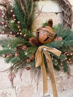 a wreath with pine cones and bells hanging on a brick wall next to a door