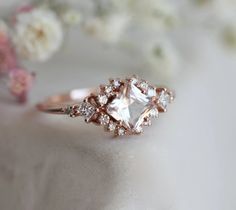 a close up of a diamond ring on a white cloth with flowers in the background