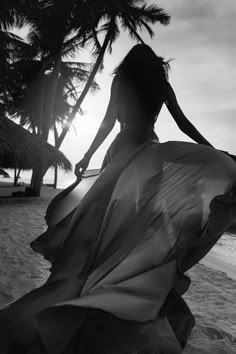 a woman in a green dress sitting on the beach at sunset with palm trees behind her