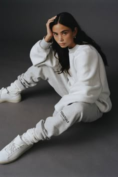 a woman sitting on the ground wearing white sneakers and sweatpants with her hands behind her head