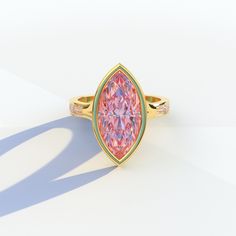 a ring with a pink diamond in the center on a white surface, it appears to be made of gold