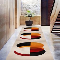 a modern hallway with an abstract rug and potted plant on the far side, along with stairs