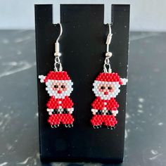 a pair of red and white beaded santa claus earrings on a black stand with a marble background