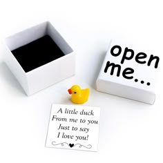 a rubber ducky sits next to an open me note on a white surface with a black box in the background