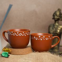 two brown coffee cups sitting on top of a burlock covered table next to a gold statue