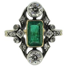 Here we have a gorgeous cluster ring dating back to the Victorian era. This antique piece has been crafted from 18ct yellow gold and showcases an elongated emerald cut emerald possessing a medium green colour tone. This focal stone has been finely milgrain set in a warm yellow gold setting at the centre of the face whilst being top and tailed by a bright white round faceted old mine cut diamond. An ornate frame acts as an open backdrop to this intense trio which is filled with much smaller yet matching old cut diamonds; all of which are set in silver. The piece is finally made complete by a neatly split band. Condition: Used (Very Good) Weight: 3.8 grams Ring Size: J (49) Band Width: 1.5mm Face Dimensions: 19.5mm x 13mm Emerald Weight: Approx. 0.86ct Total Centre Diamonds Weight: Approx. 0 Luxury Victorian Emerald Ring With Rose Cut Diamonds, Victorian Emerald Cut Emerald Jewelry, Victorian Style Collectible Emerald Ring, Victorian Emerald Collectible Ring, Luxury Vintage Emerald-cut Cluster Ring, Victorian Diamond Ring, Double Heart Ring, Emerald Diamond Ring, La Face