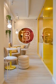 the interior of a restaurant with yellow and white chairs, tables and round mirrors on the wall