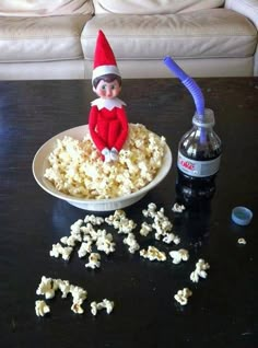 an elf sitting on top of a bowl of popcorn next to a bottle of soda