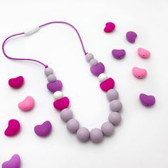 an assortment of pink and purple necklaces on a white surface with hearts attached to the beads