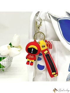 a white purse with a red and yellow keychain hanging from it's side