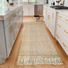 a kitchen with white cabinets and gold handles on the countertops, along with a beige runner rug