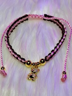 a pink and black beaded bracelet with a gold teddy bear charm hanging from it