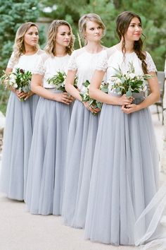 a group of women standing next to each other wearing long gray skirts and holding bouquets