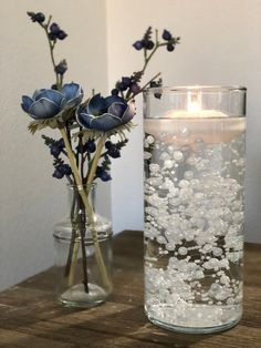 two vases filled with water and flowers on a table next to a lit candle