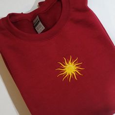 a red t - shirt with yellow sun embroidered on the front and back, sitting on a white surface