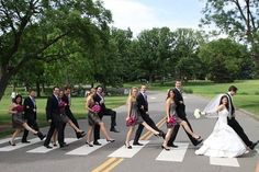 a bride and groom crossing the street in front of their wedding party