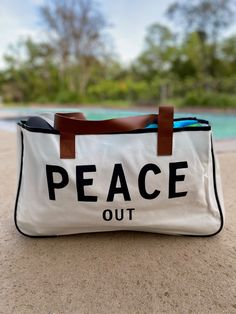 Tote around your daily essentials in this super chic PEACE OUT large canvas tote bag! Sling this bad boy over your shoulder as you go about your day, stylishly proclaiming your inner chill and total mindfulness. With its large size, you can fit everyone's needs in one bag (talk about making peace)! Perfect for weekend getaways, lake days, beach days and more! Made of canvas and brown vegan leather 20" wide 11" tall 5" deep Trendy Canvas Beach Bag For Everyday Use, Trendy Canvas Weekender Bag For Everyday Use, Casual White Weekender Bag With Leather Handles, Casual Canvas Bags For Weekend, Casual White Tote Travel Bag, Trendy White Weekender Bag For Everyday Use, Casual Canvas-lined Shoulder Bag For Weekend, Trendy Canvas Shoulder Weekender Bag, Casual Shoulder Bag With Canvas Lining For Weekend