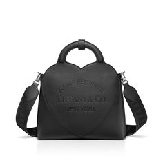 Inspired by one of the House’s most distinctive designs, the heart-shaped Return to Tiffany® handbags are crafted in supple leather that nod to our iconic jewelry. This small tote adds a playful touch to every day. It’s embossed with our signature heart motif and designed with a detachable woven strap, while an interior zip pocket keeps essentials organized. Black Taurillon leather; 11.4 x 13.7 x 4.3"; Detachable woven strap and fixed handles; Interior zip pocket; Flap closure with magnet; Cotton-blend lining; Comes with dust bag; Made in Italy | Return to Tiffany® Small Tote Bag in Black Leather Iconic Jewelry, Accessory Inspo, Return To Tiffany, Leather Tote Bags, Heart Motif, Classic Handbags, Small Tote Bag, Tote Bag Leather, Leather Shops