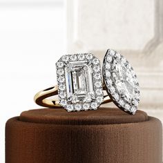 two engagement rings sitting on top of a brown velvet ring box with a white diamond in the center