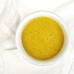 a white cup filled with yellow liquid on top of a white cloth covered tablecloth