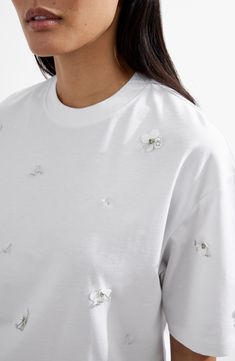 Sparkly, embellished flower appliqués add textural elegance to this boxy T-shirt made from soft cotton. 26" length Crewneck Short sleeves 100% cotton Dry clean or machine wash, dry flat Made in Turkey White Embellished Crew Neck T-shirt, White Embellished Crew Neck Top, White Floral Embellished Tops For Summer, White Crew Neck T-shirt With Floral Applique, White Embellished Cotton Tops, White Short Sleeve T-shirt With Floral Applique, Spring Embellished Crew Neck T-shirt, Embellished Crew Neck T-shirt For Spring, Casual Embellished Crew Neck T-shirt