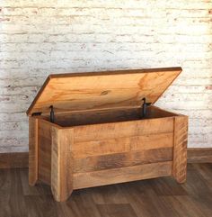 an empty wooden box sitting on top of a hard wood floor next to a brick wall