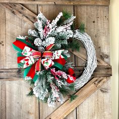 a christmas wreath hanging on the side of a wooden door with red and green bows