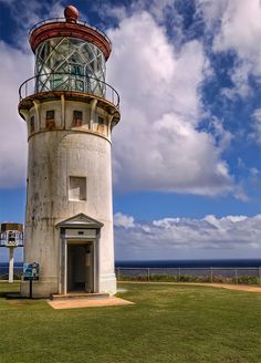 an old light house sits in the middle of a grassy area with a blue sky and white clouds