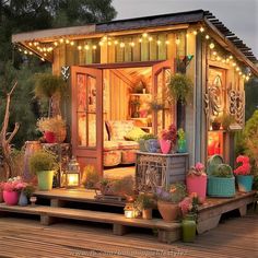 a tiny house is lit up with fairy lights and potted plants on the porch