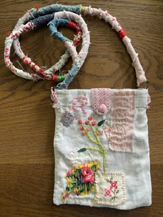 a handbag with flowers and beads on it sitting on a wooden table next to another bag