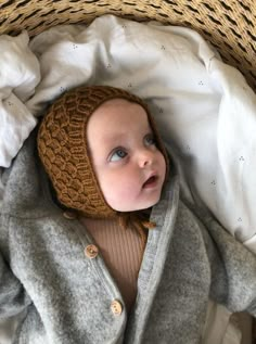 a baby wearing a knitted hat laying in a basket