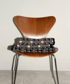 a wooden chair with black and white patterned cushion on top of it, against a white wall