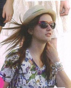 a woman wearing sunglasses and a hat with her hair blowing in the wind while standing next to other people