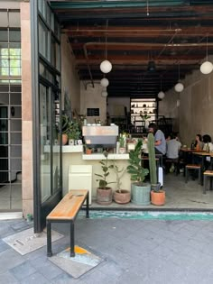 people sitting at tables in an outdoor cafe with potted plants on the outside wall