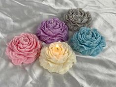 four different colored flowers sitting on top of a white sheet with a lit candle in the middle