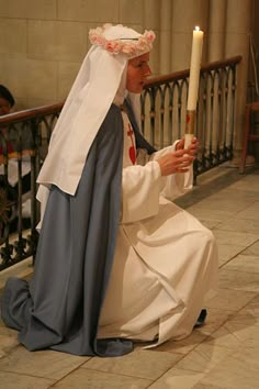 a man sitting on the ground holding a candle in his hand and wearing a priest's outfit