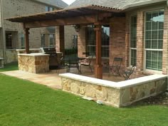 a patio with an outdoor kitchen and dining area in the back yard, next to a brick building