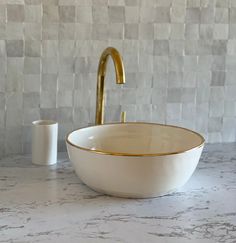 a white bowl sink sitting on top of a counter next to a gold faucet