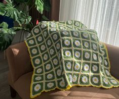 a crocheted blanket sitting on top of a couch next to a potted plant