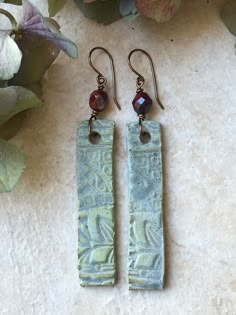 pair of green earrings with red glass beads on white surface next to flowers and leaves