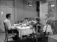 an old black and white photo of people sitting at a dining room table eating food