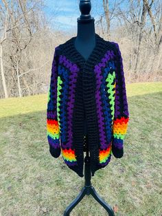 a colorful crocheted jacket is on a mannequin in the grass with trees in the background