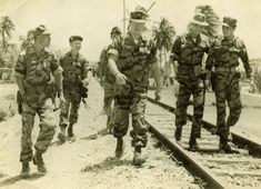 an old black and white photo of men in uniforms walking on train tracks with palm trees behind them