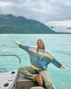 a woman sitting on top of a boat in the water with mountains in the background