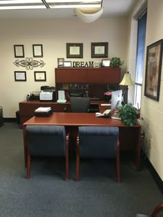 an office cubicle with two desks, chairs and pictures on the wall above them