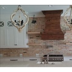 a kitchen with white cabinets and an old fashioned stove hood over the range in front of two chandeliers