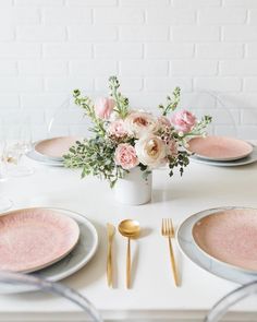 the table is set with pink and white plates, silverware, and floral centerpieces