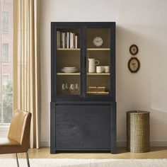 a black bookcase with glass doors in a living room next to a chair and window