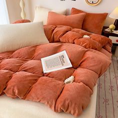 an orange comforter on top of a bed with pillows and a book laying on it