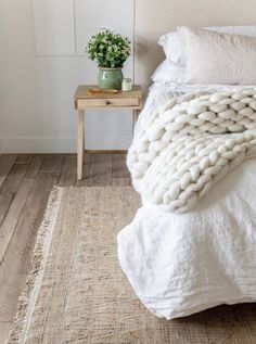 a bed with a white blanket on top of it next to a small wooden table